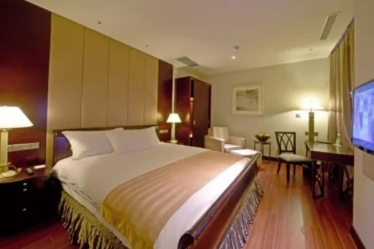 A hotel room with a large bed, bedside tables, a desk, and a television.