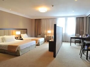 A hotel room with two beds, a desk, a chair, and a television.