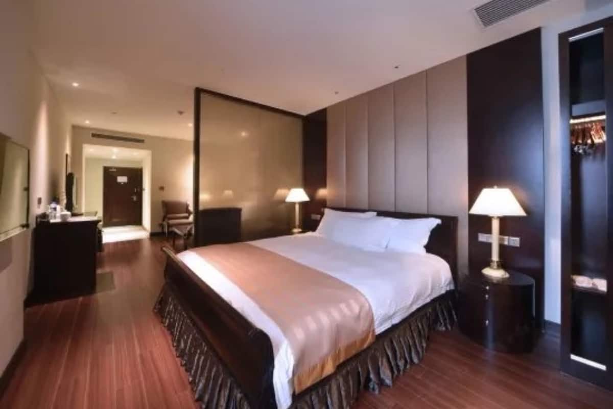 A modern hotel room with a large bed, bedside tables, a wardrobe, and a mirror.
