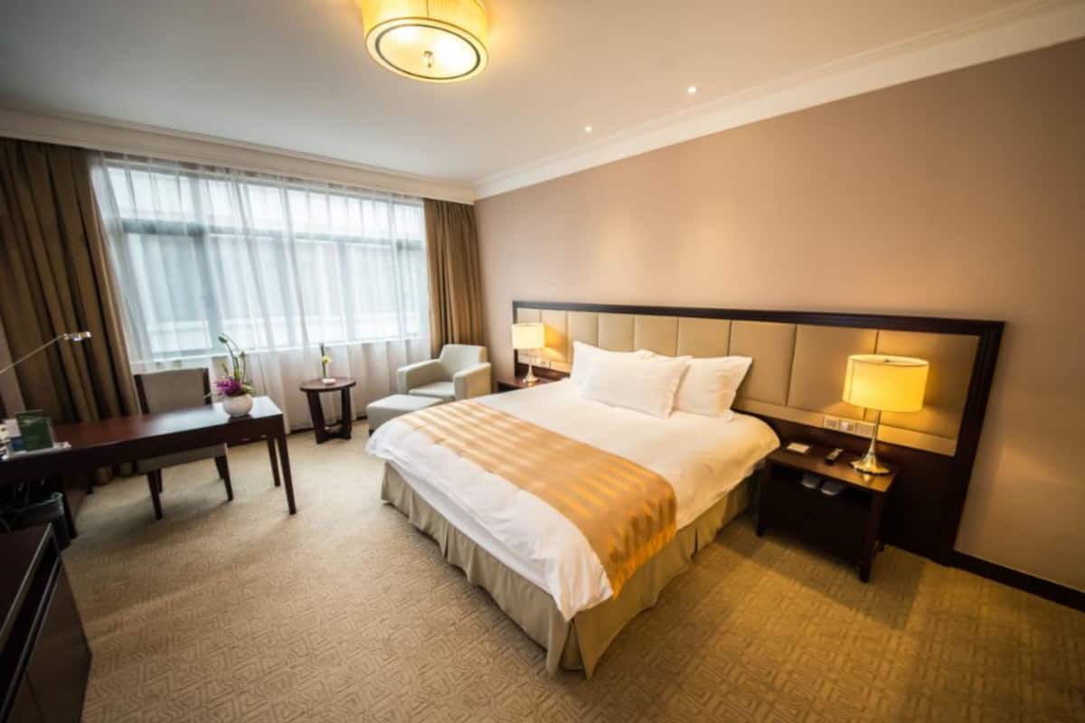 A hotel room with a large bed, two bedside tables with lamps, a desk with a chair, and a window with curtains.