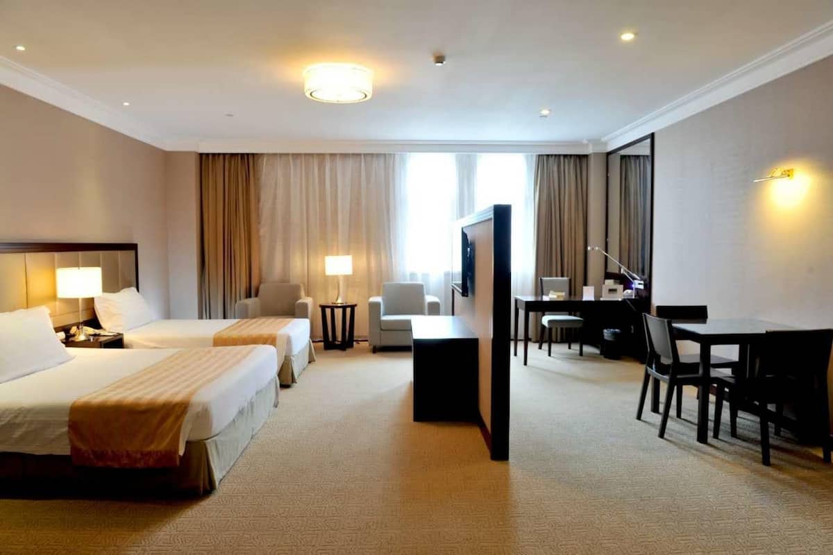A hotel room with two beds, a desk, a chair, a TV, and a lamp.