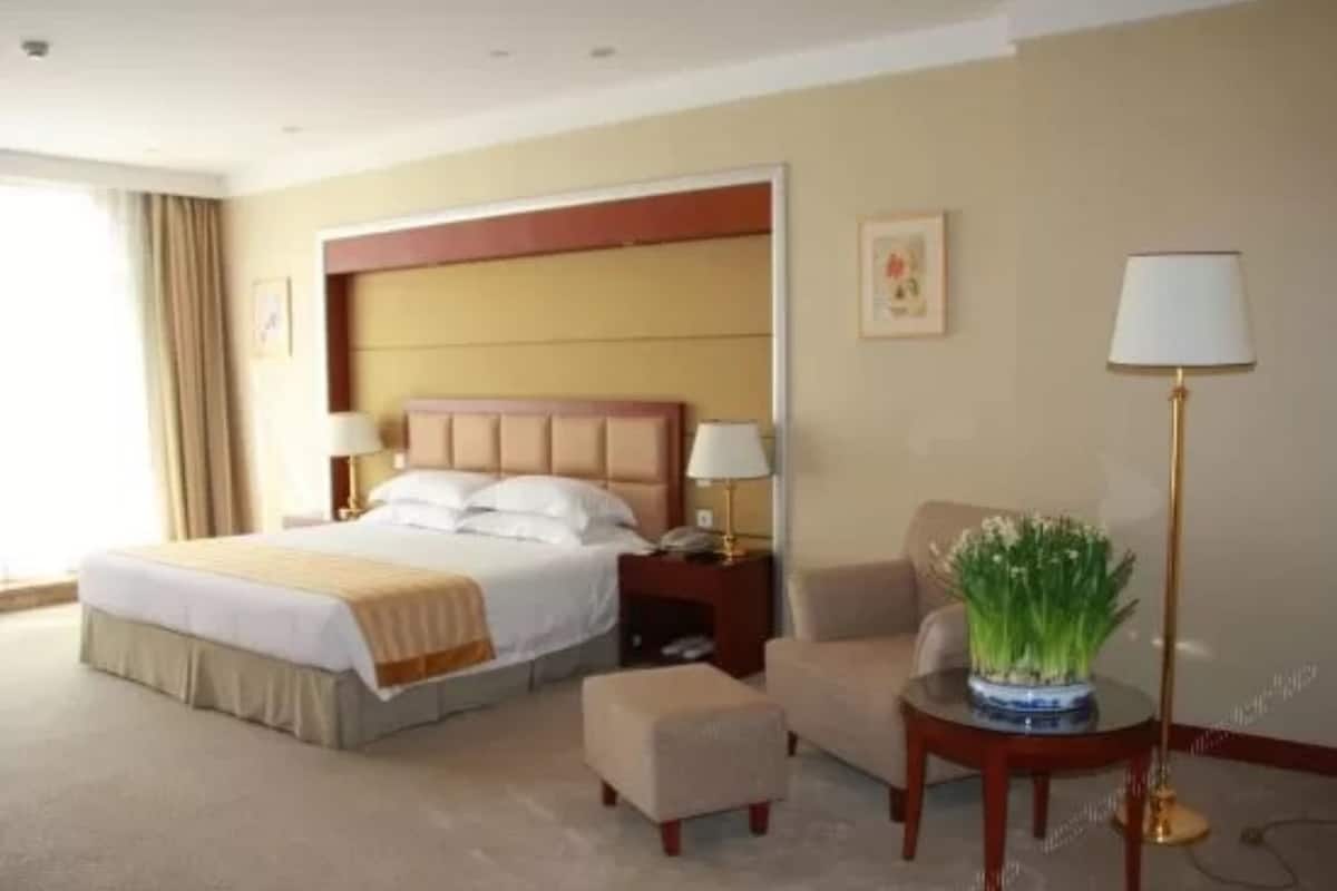 A hotel room with a large bed, a bedside table, a chair, a small table with a lamp, and a vase with flowers.