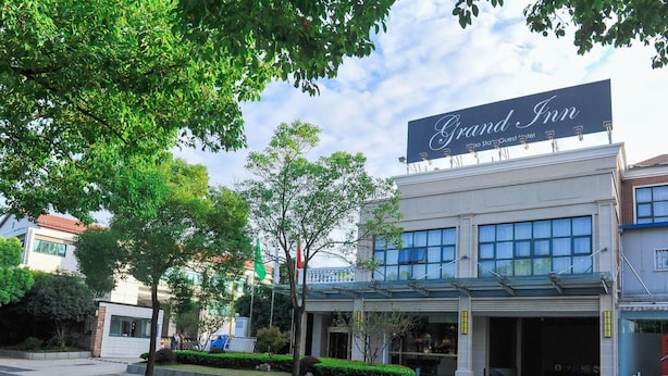 A Grand Inn hotel with a prominent sign, a covered entrance, and a parking area. - Grand Inn Xijiao State Guest Hotel (Shanghai)
