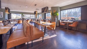 Un restaurante espacioso con techos altos, ventanas grandes y diversas opciones de asientos, incluyendo cabinas y mesas.