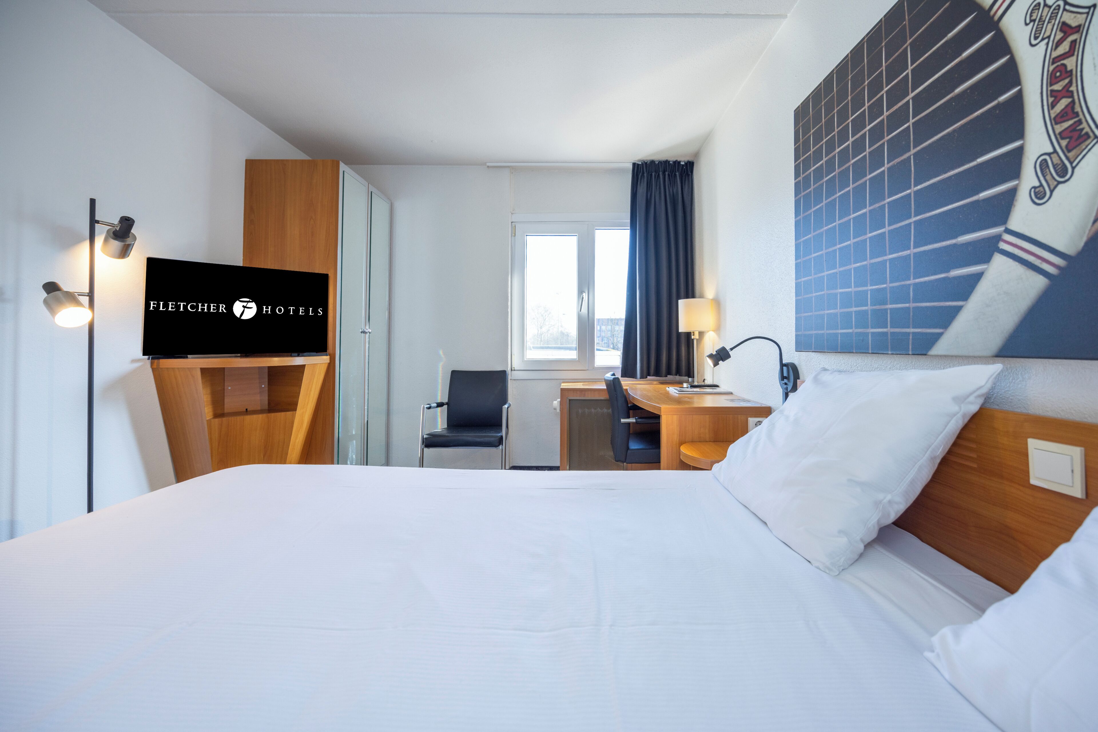 A hotel room with a bed, a desk, a chair, a television, and a window with curtains.