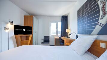 A hotel room with a bed, a desk, a chair, a television, and a window with curtains.