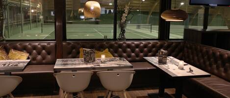 Un restaurante moderno con una zona de asientos en cabinas de cuero, sillas blancas y una mesa con una vela.