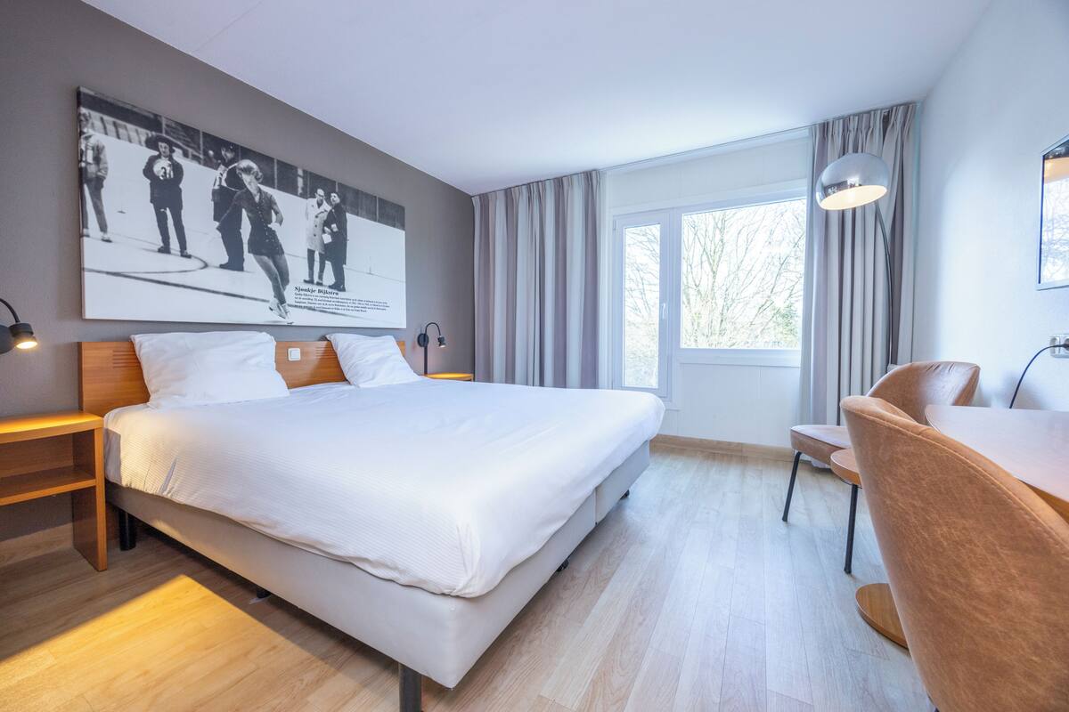 Una habitación de hotel moderna con una cama grande, un escritorio y un ventanal con cortinas.