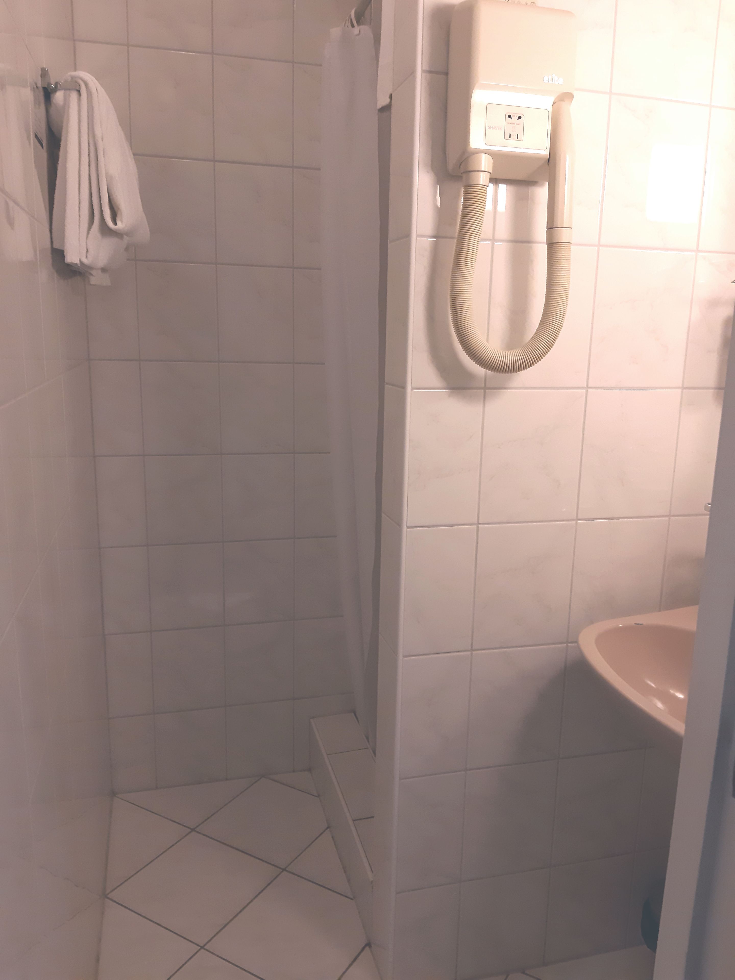 A bathroom with white tiles, a shower, a toilet, and a towel rack.