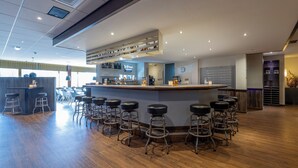 Zona de bar con taburetes, barra y estantería con botellas.