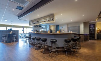Zona de bar con taburetes, barra y estantería con botellas.