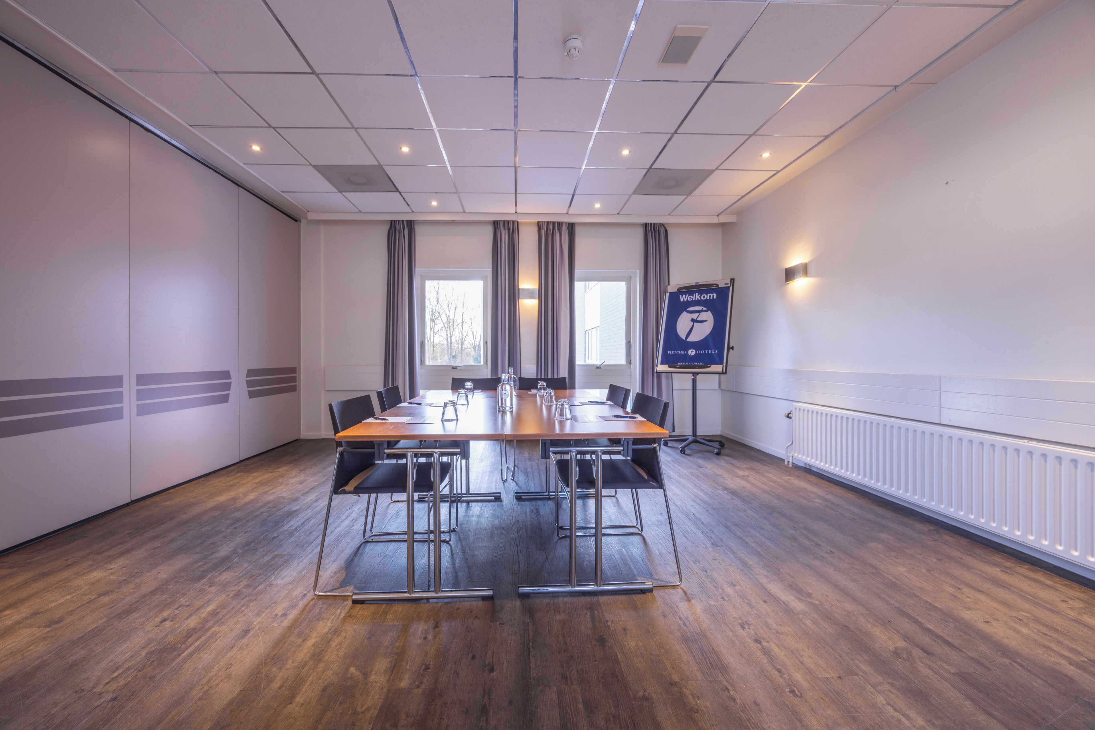Un salón de conferencias con una mesa larga, sillas y un cartel de 'Welcome'.