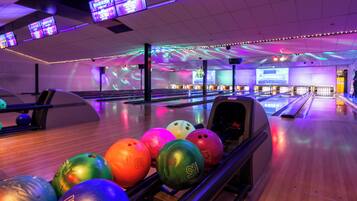 A bowling alley with multiple lanes, bowling balls, and overhead screens displaying advertisements.