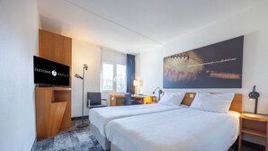 Habitación de hotel con dos camas, televisión, escritorio, lámpara y un cuadro grande en la pared.