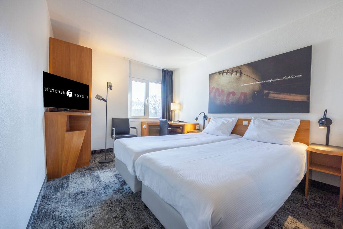 Habitación de hotel con dos camas, televisión, escritorio, lámpara y un cuadro grande en la pared.