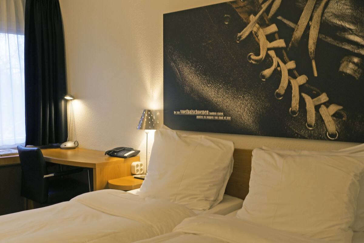 Habitación de hotel con cama, escritorio, silla, lámpara y una obra de arte grande en la pared.