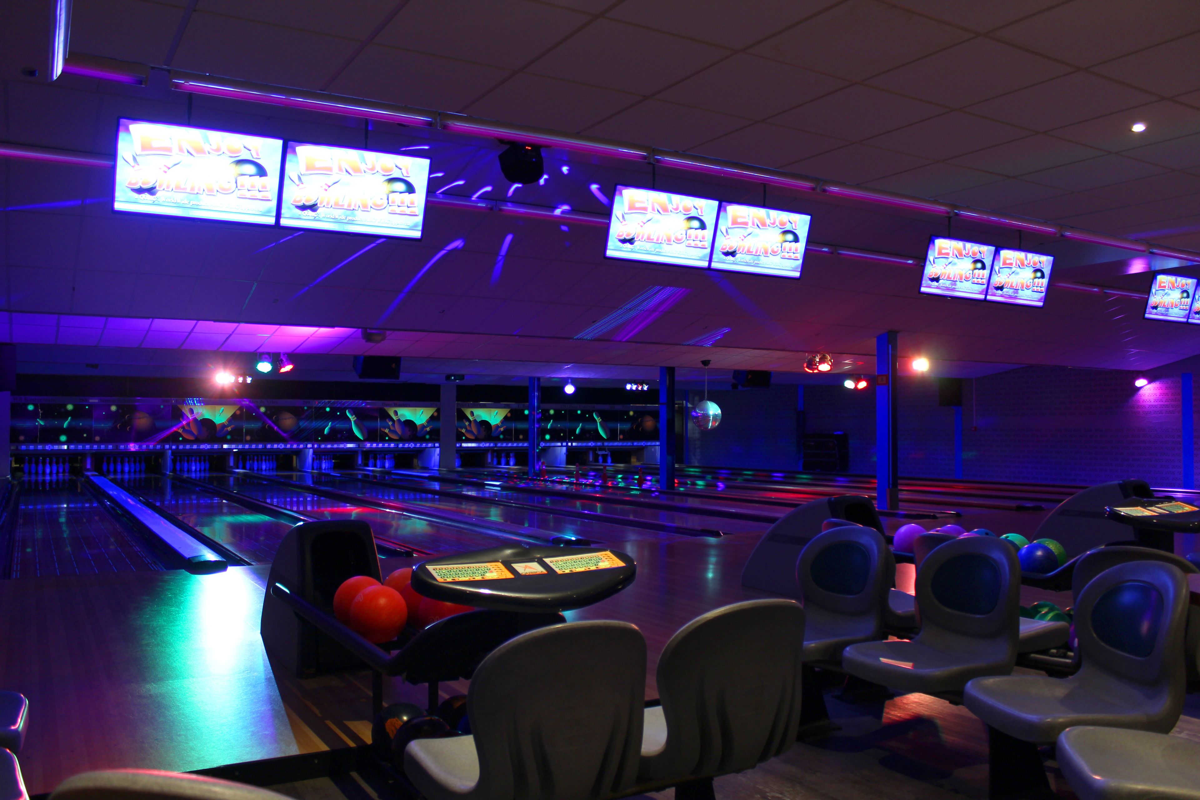 Uma pista de boliche com várias pistas, luzes neon e diversas bolas de boliche.