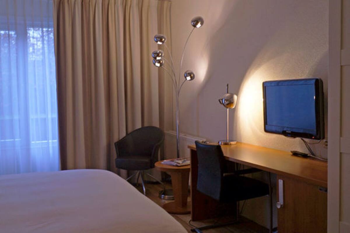 Una habitación de hotel con cama, escritorio, silla, lámpara de escritorio y televisor.
