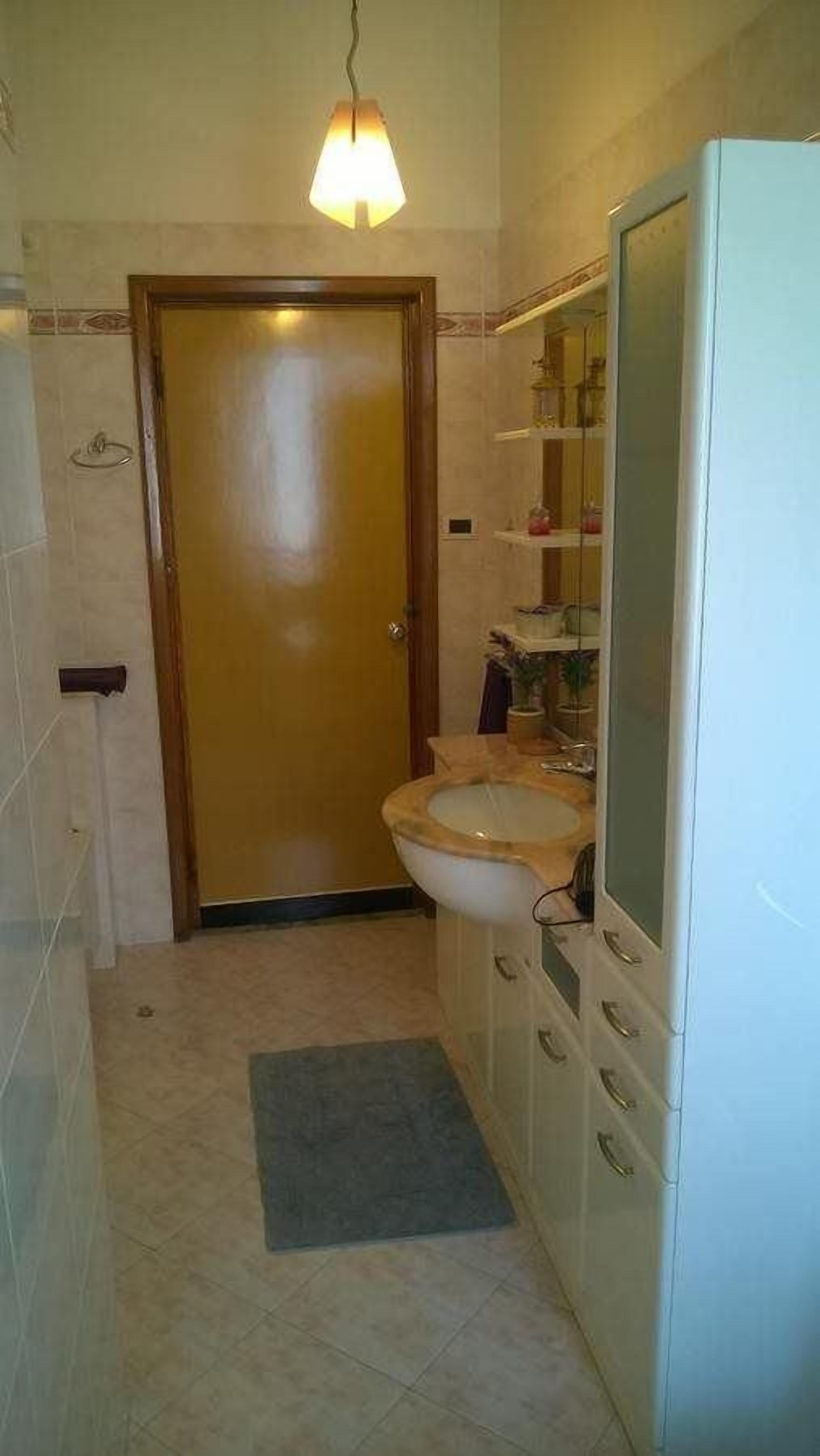 A small bathroom with a toilet, sink, and a mirror. There is a door leading to another room and a small rug on the floor.