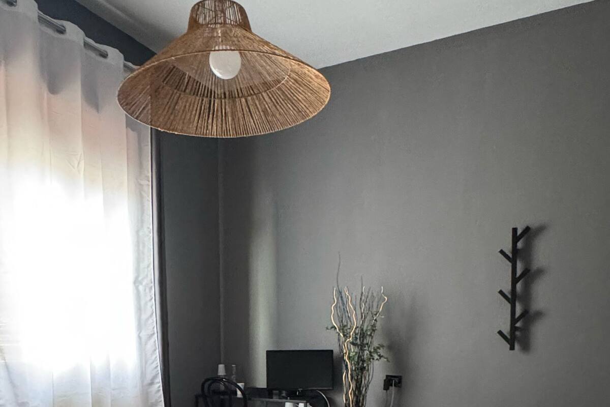 Une chambre à coucher comprenant un lit, un luminaire suspendu, un bureau avec une chaise, un téléviseur et un porte-manteau fixé au mur.