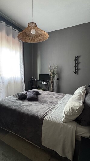 A bedroom with a bed, a hanging light fixture, a desk with a chair, a television, and a wall-mounted coat rack. - B&B Frontepista (Pescara)