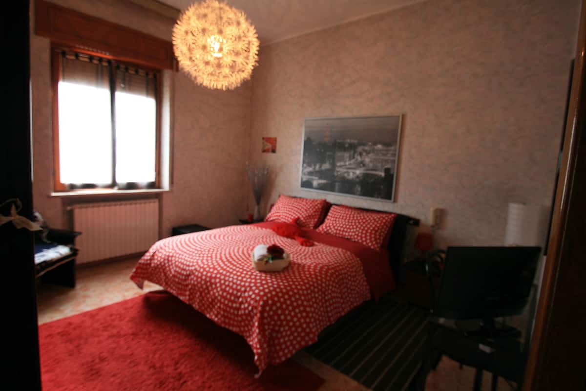 Une chambre à coucher comprenant un lit, une chaise, un bureau, une fenêtre avec des rideaux, un radiateur et un tableau accroché au mur.