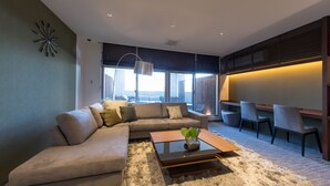 A modern living room with a sectional sofa, a coffee table, and a view of the outdoors. - Rota Hostel (Osaka)