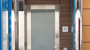 A modern elevator with a metallic finish, a wooden panel, and a sign indicating "m's BLD." - Rota Hostel (Osaka)