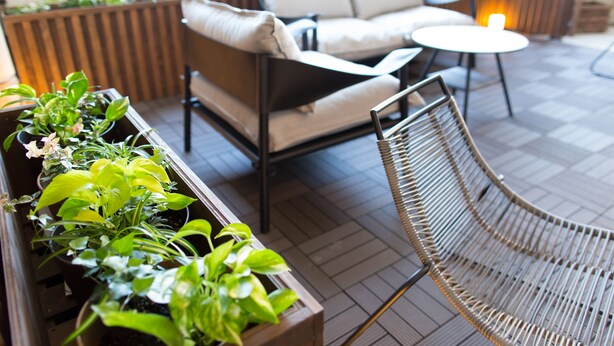A modern outdoor seating area with a sofa, a round table, and a metal chair. There are potted plants along the seating area. - Rota Hostel (Osaka)