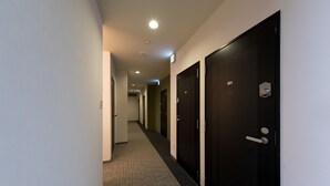 A hotel hallway with dark doors, a carpeted floor, and recessed lighting. - Rota Hostel (Osaka)