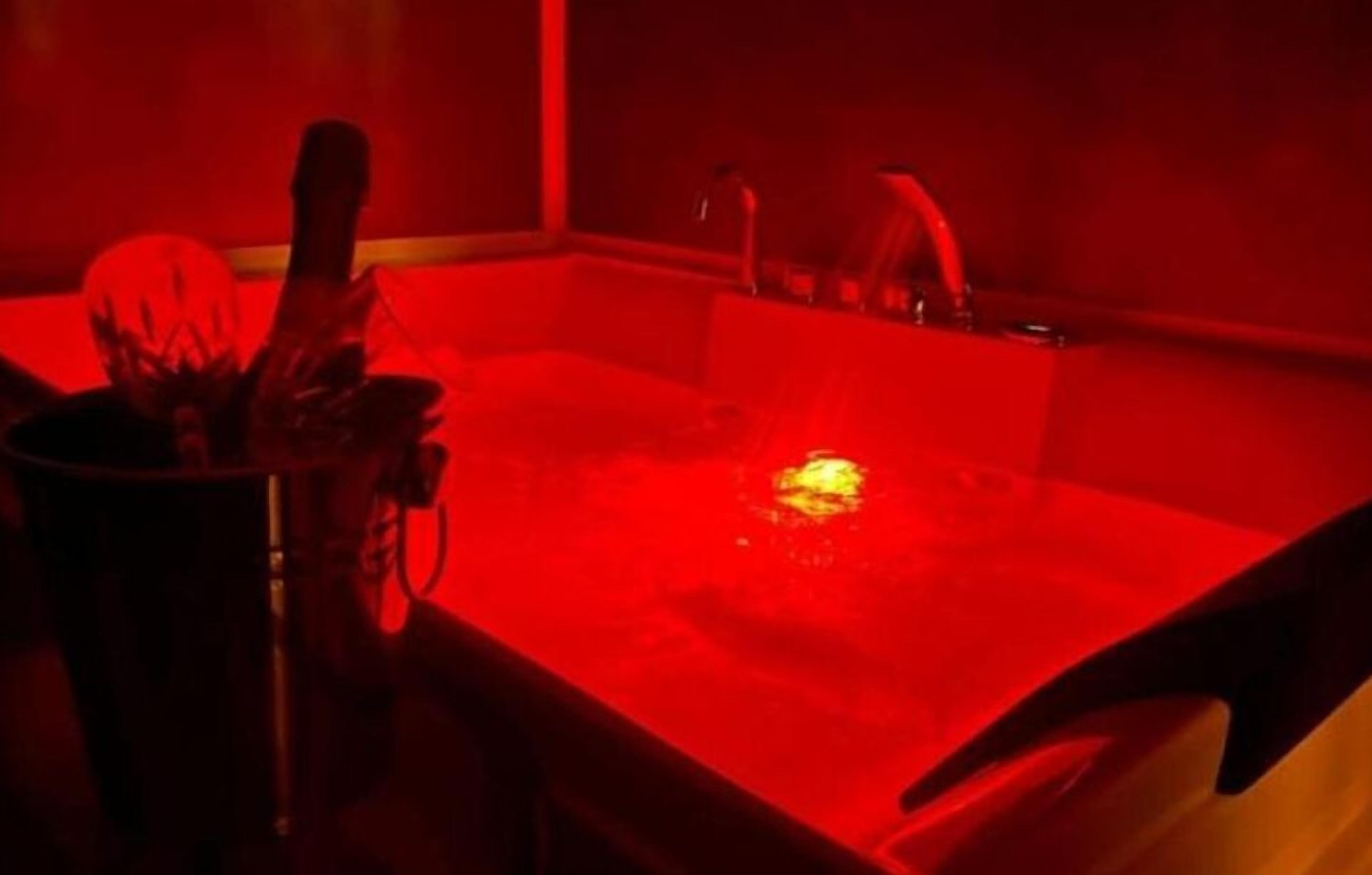 A red-lit room with a bathtub, a sink, and a metal container.