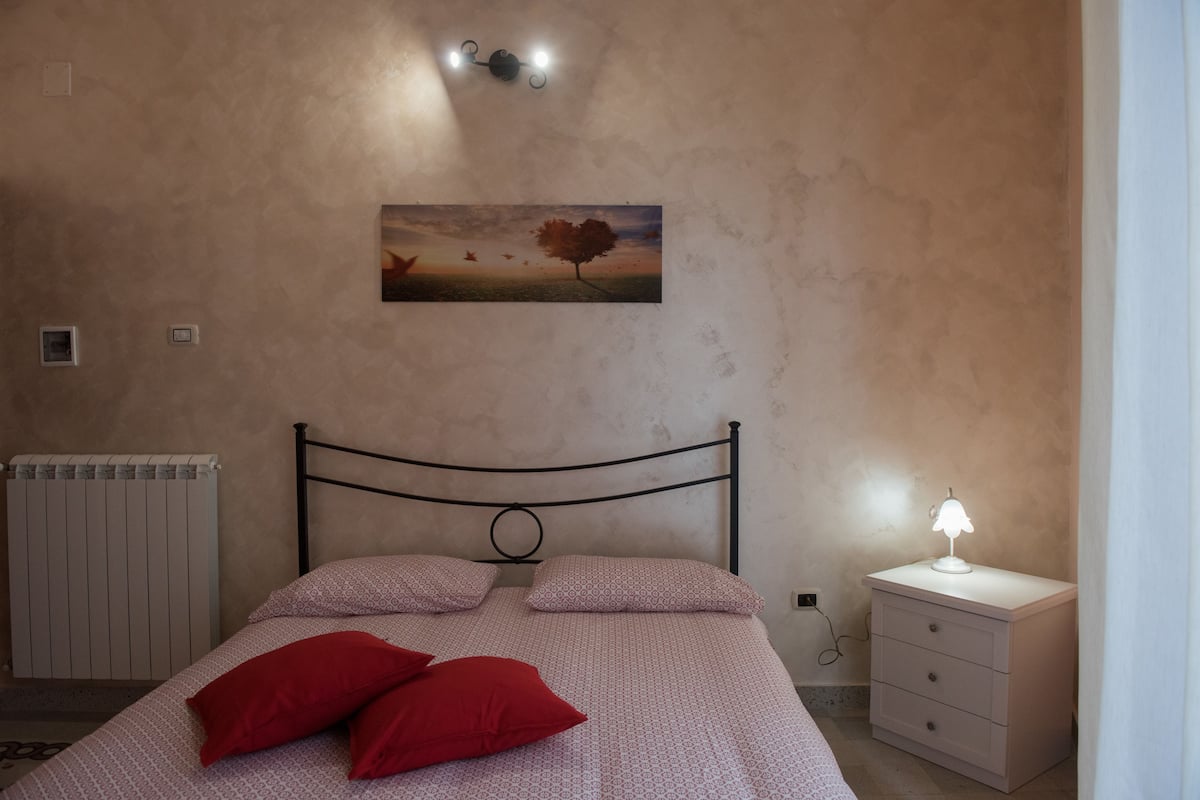 Ein Schlafzimmer mit einem Bett, einem Nachttisch, einer Wandlampe, einer Heizung und einem Gemälde.