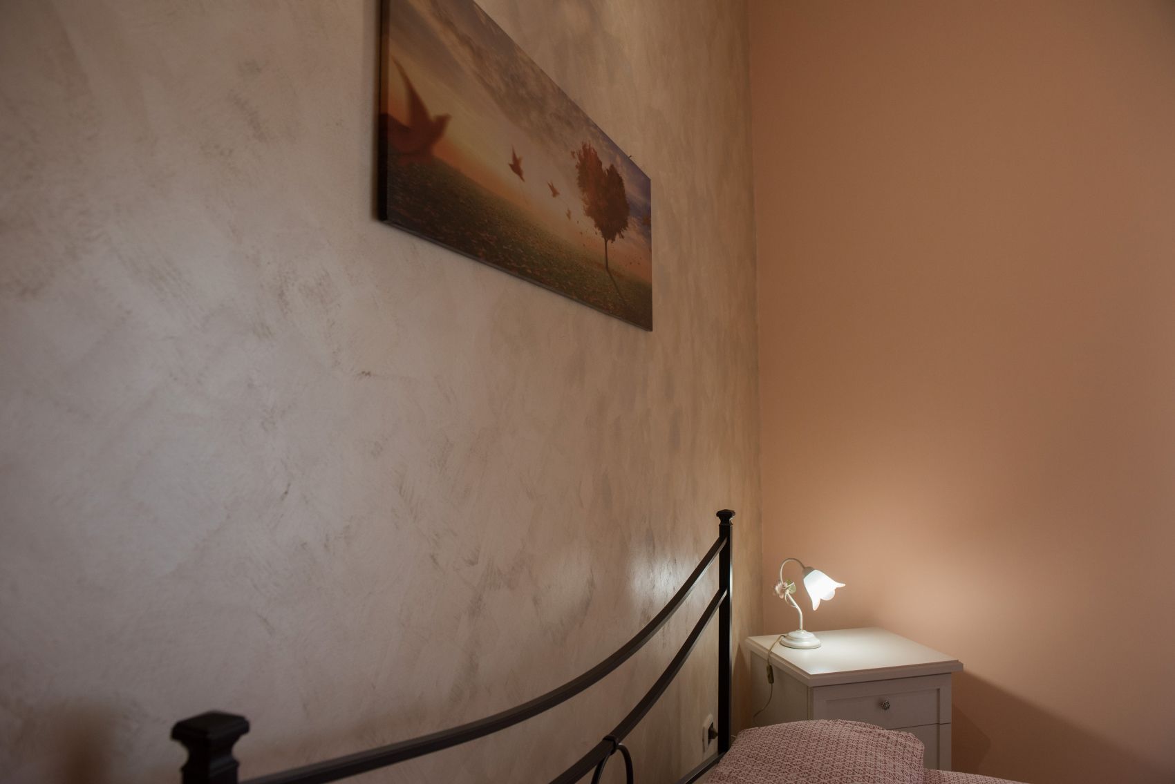 A bedroom with a bed, a nightstand, a lamp, and a painting on the wall.