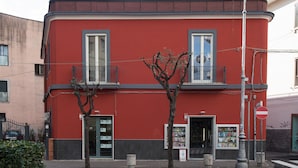 A red building with two windows and a door, a small tree in front, and a street sign. - B&b Viatrento30 (Salerno)