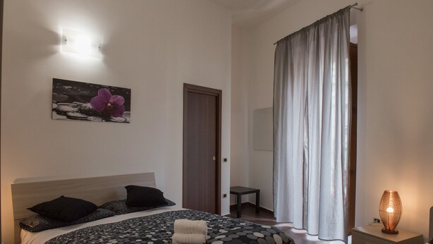 A bedroom with a bed, a bedside table, a nightstand, a painting, and a window with curtains. - B&b Viatrento30 (Salerno)