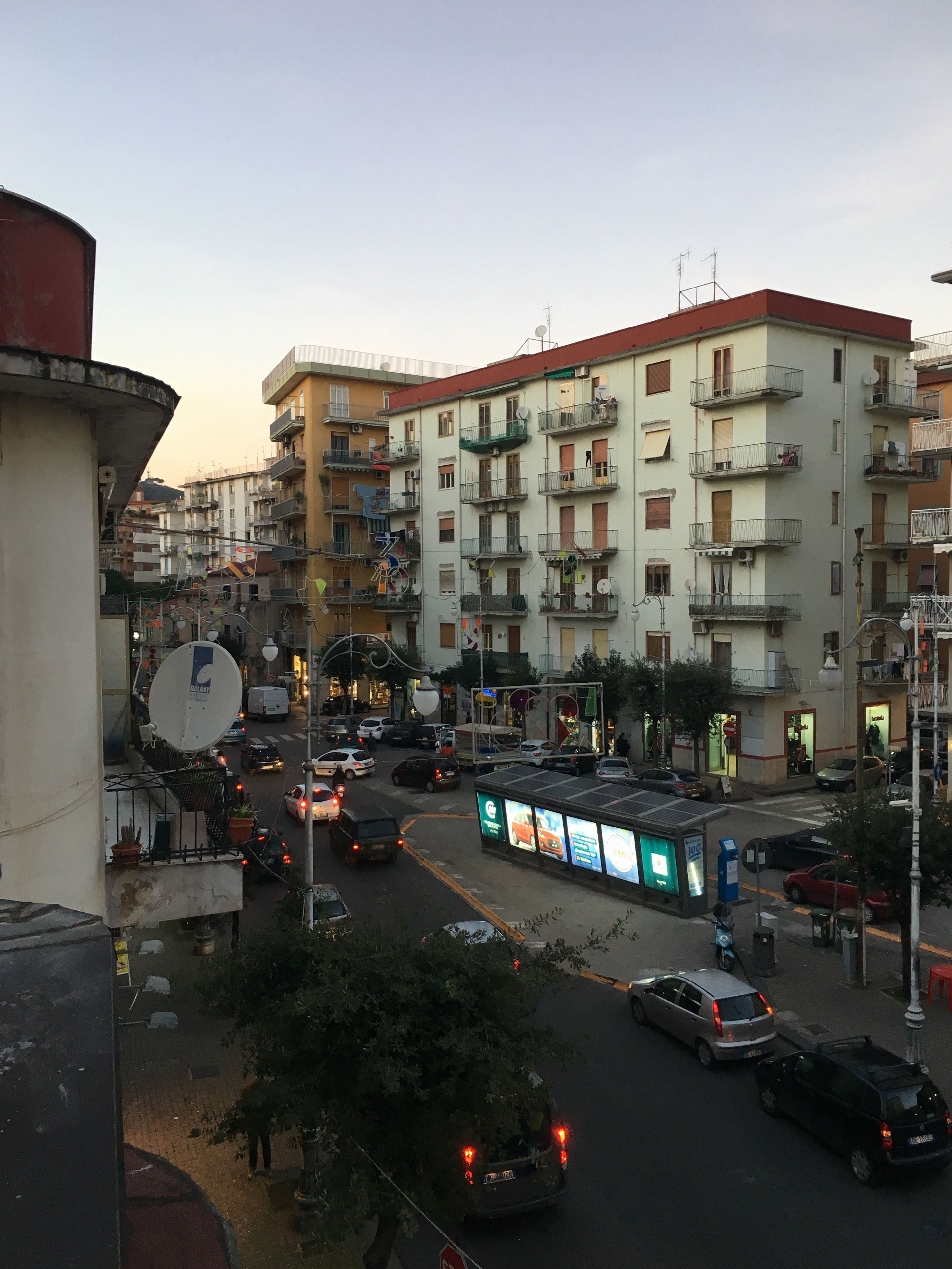 A multi-story building with balconies, a street with cars, and a bus stop with advertisements.