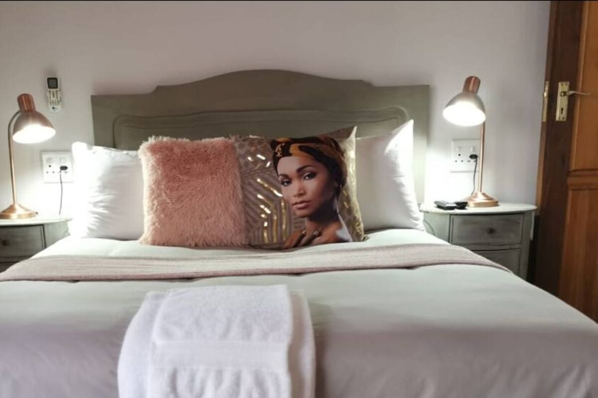 A neatly made bed with white linens, two bedside lamps, and a wooden wardrobe in the background.