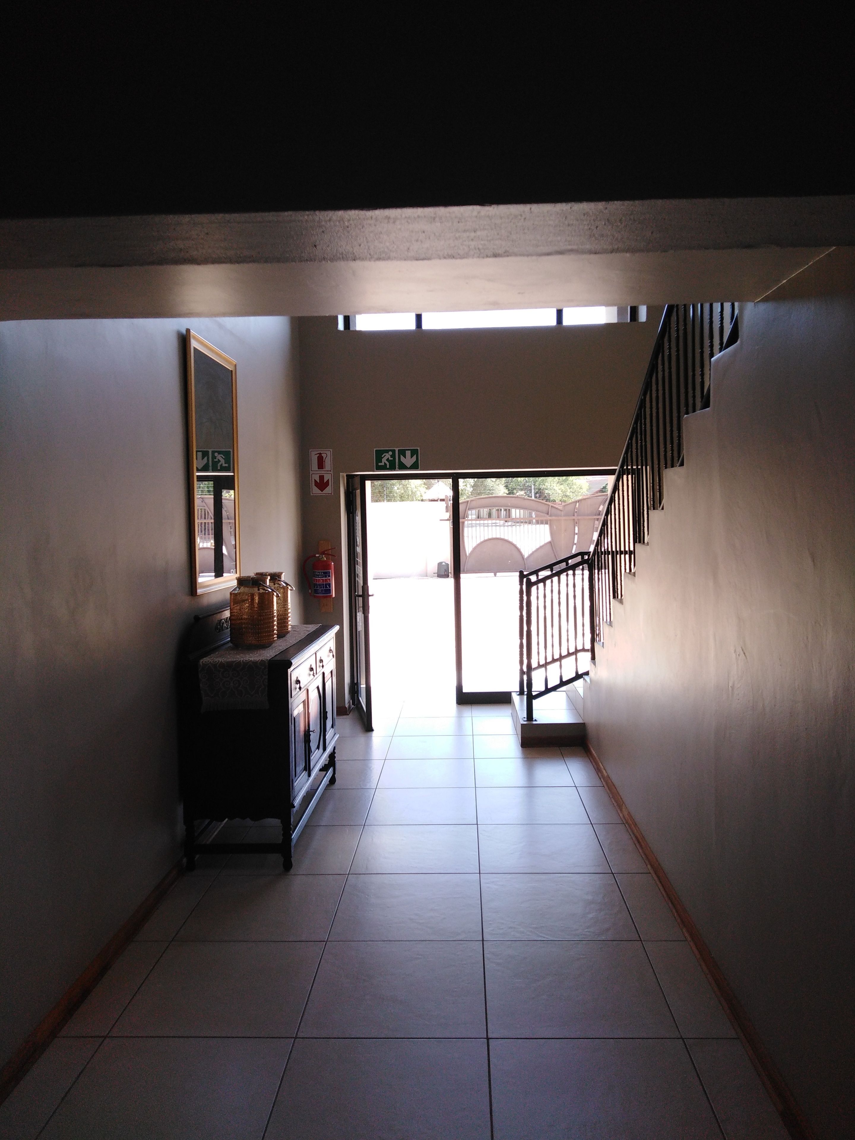 A hallway with a staircase leading to an outdoor area. There is a fire extinguisher and emergency exit signs on the wall.