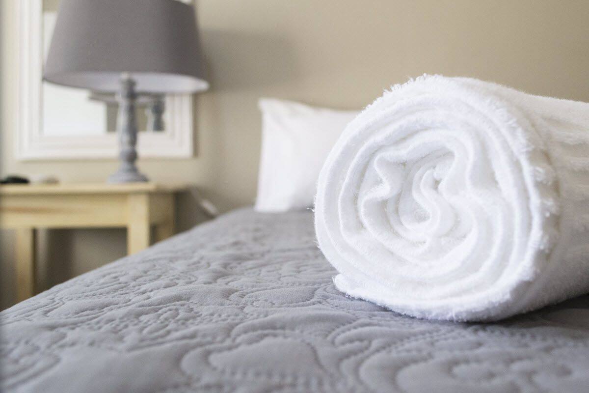A neatly made white towel on a bed with a textured white bedspread.