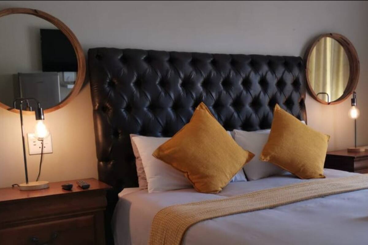 A hotel room with a tufted headboard, two bedside tables with lamps, a bed with white linens and two mustard-colored pillows, and two round mirrors on the walls.