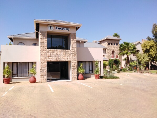 A Tuscany hotel with a stone facade, a prominent entrance, and a parking lot. - Tuscany Boutique Hotel (Vryburg)
