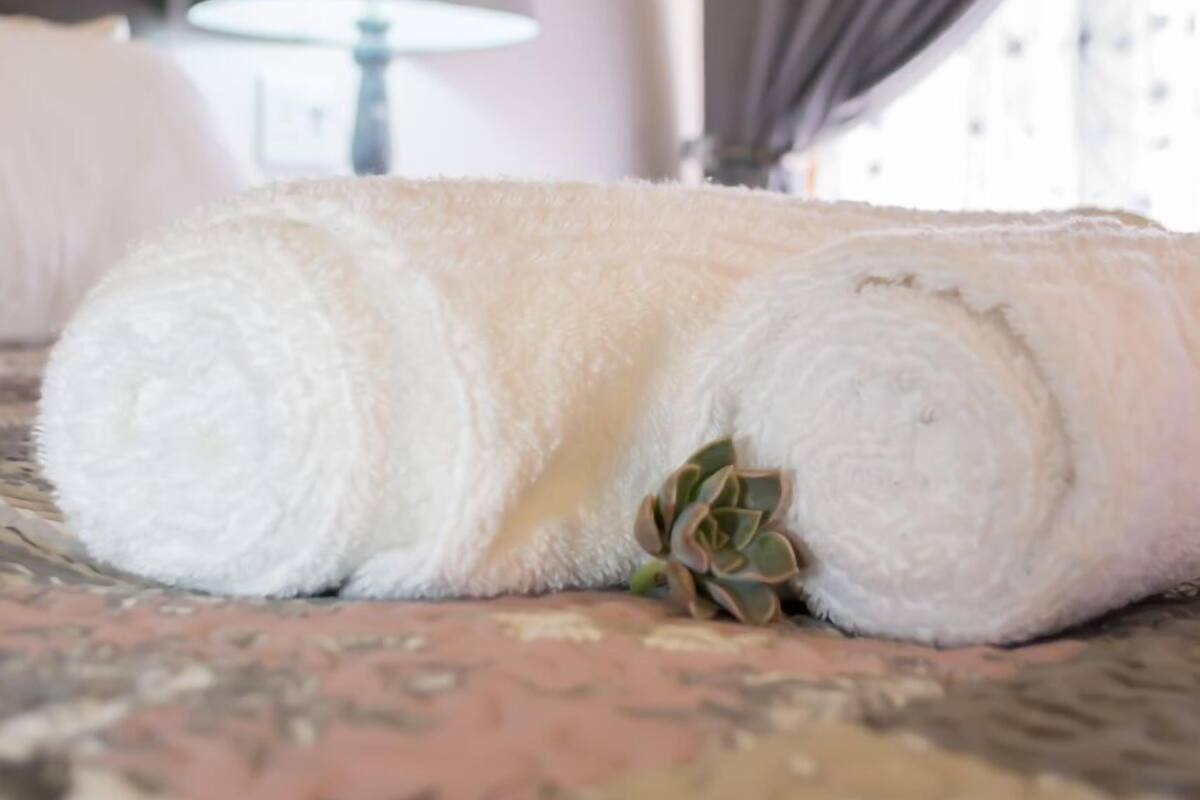 A neatly rolled white towel on a bed with a patterned bedspread.