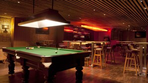 A pool table with a green felt surface, surrounded by bar stools and a bar area with a television mounted on the wall. - Lemon Tree Hotel Banjara Hills (Hyderabad)