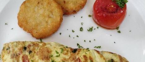 Um prato com omelete, duas panquecas de batata e tomate.