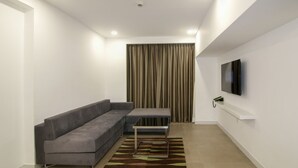 A modern living room with a grey sectional sofa, a small table, and a television on the wall. - Lemon Tree Hotel Banjara Hills (Hyderabad)