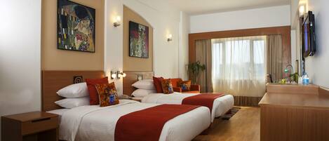 A hotel room with two beds, a wooden desk, a ceiling fan, and artwork on the walls.