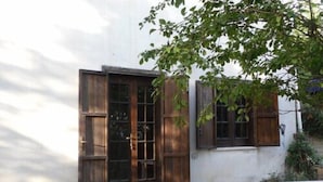 A rustic building with a wooden door and window shutters, a small outdoor seating area, and a tree providing shade. - Le Dieci Querce (Tortorella)