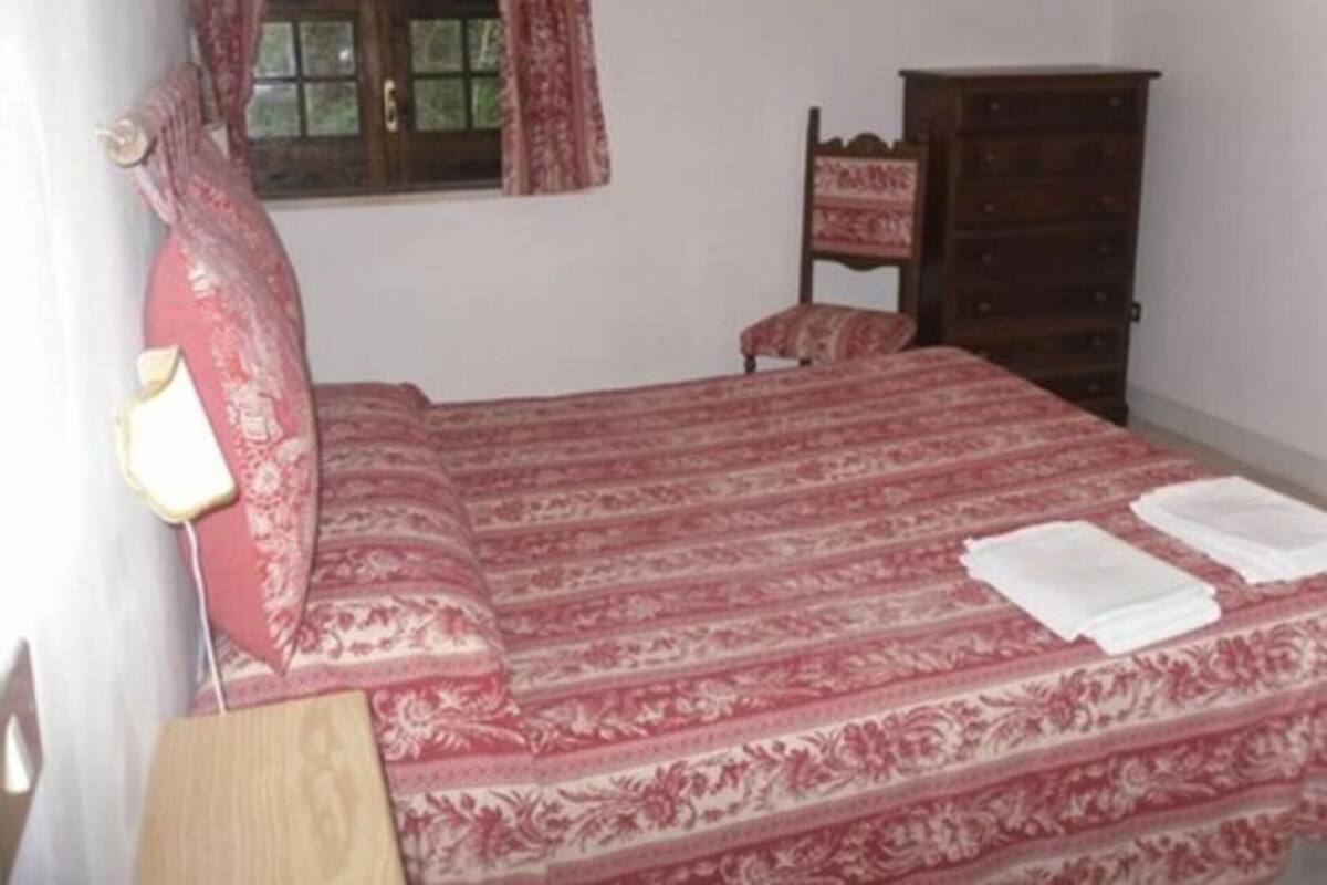 Ein Schlafzimmer mit einem Bett, einer Holzkommode, einem Nachttisch und einem Fenster mit Vorhängen.