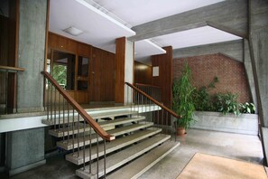 Uma escadaria com corrimãos de madeira e piso de concreto, que leva a um patamar com uma planta em vaso.