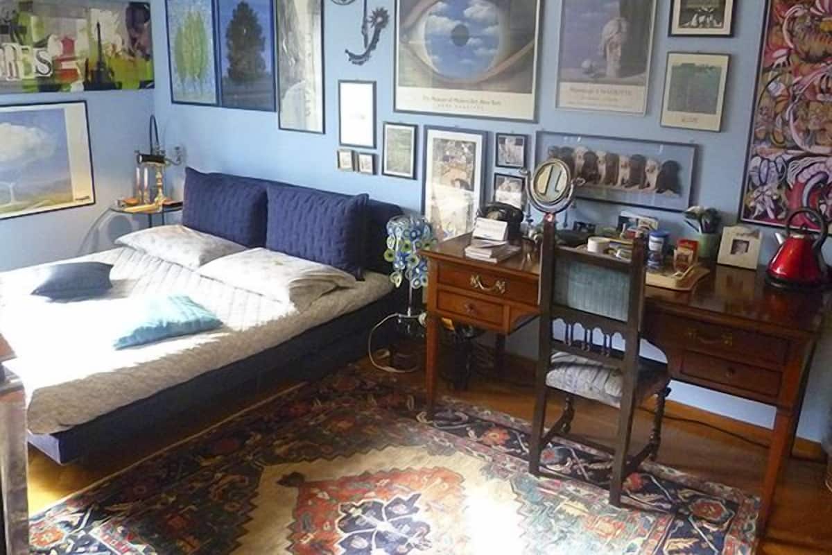A bedroom with a bed, dresser, desk, and a wall adorned with framed pictures.